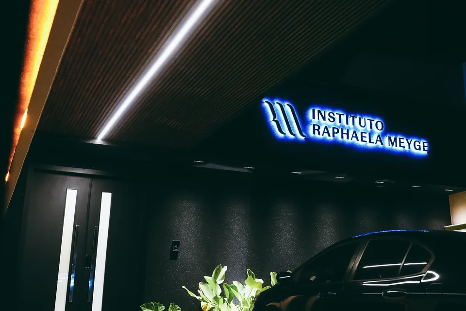 Fachada do Instituto Raphaela Meyge à noite, com o letreiro azul iluminado sobre a entrada